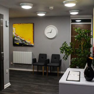 White door in hallway with clocks and two black chairs and white clock hanging above