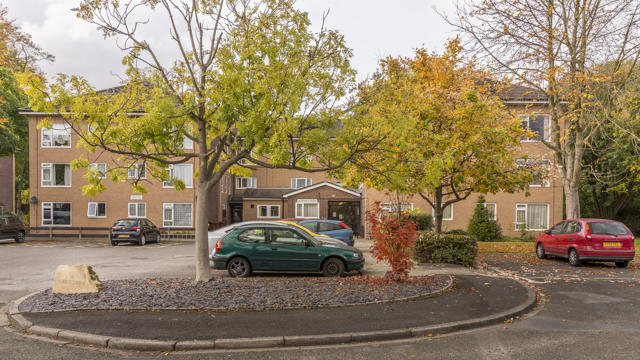 Front of Alderfield property with cars parked and trees in the garden