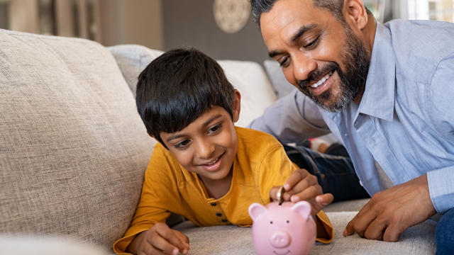 Man and son putting a coin in a piggybank 