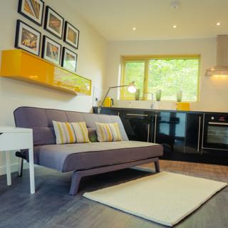 Grey couch with white cushions with a black coloured kitchen in the background