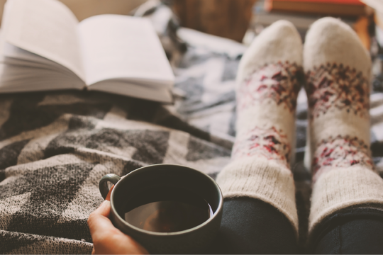 A woman in cosy socks with a cup of tea reading a book 
