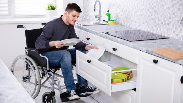 Man in wheelchair putting his dished into the cupboard 