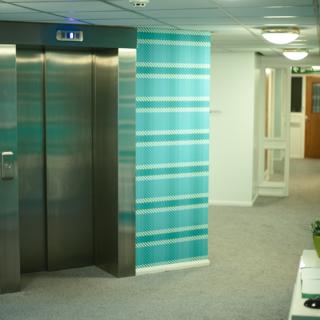 Picture of a lift with a hallway in the background which leads to a brown door