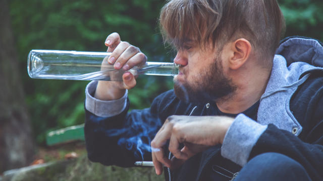 Man in blue jacket drinking and smoking at the same time 