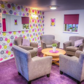Four grey chairs in a very colourful pink room with a patterned wallpaper