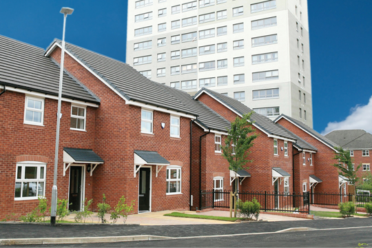 Four houses in a row with a black door with a high rise flat in the background