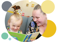 Woman laughing with her daughter whilst reading a book.