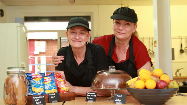 Two workers at the café and different food choices in front of them