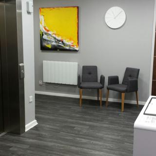 White door in hallway with clocks and two black chairs and white clock hanging above