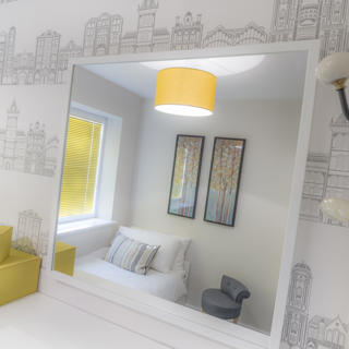 Mirror reflecting a white chair and yellow lamp shade hanging from the ceiling