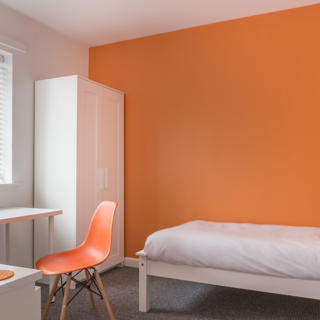Room with orange wallpaper with white bed and desk