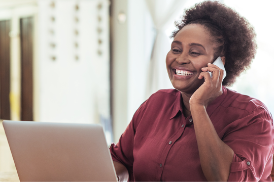 A woman on the phone smiling whilst looking at her laptop 