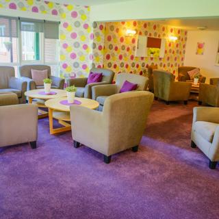 Lots of grey chairs in a very colourful pink communal room with a patterned wallpaper
