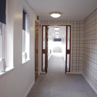 Hallway with open windows to the left and a patterned wallpaper to the right 