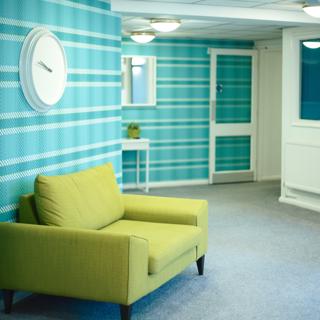 Green chair in front of a white clock and a blue patterned wall
